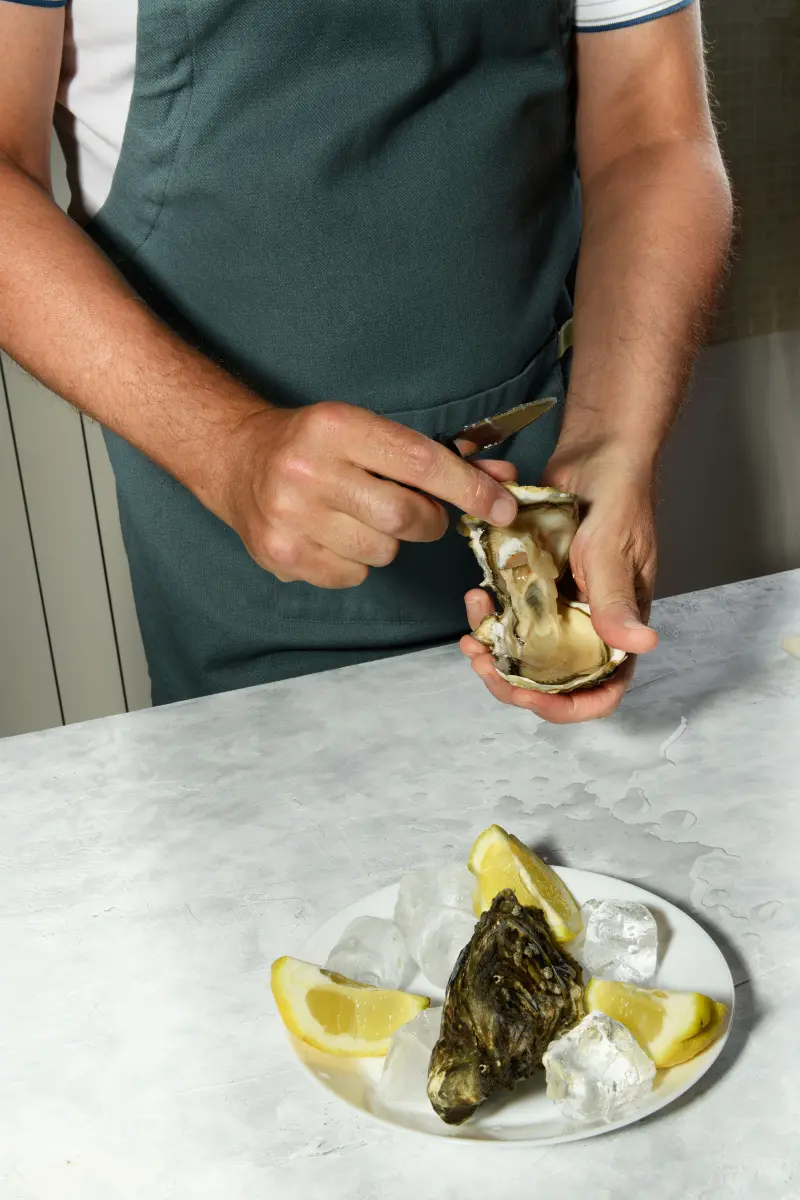 Freshly opened oyster being finished with a squeeze of lemon over the shell