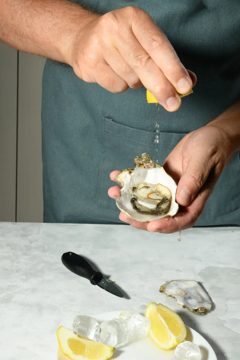 Final oyster presentation with shell on ice and lemon wedges after safe shucking technique